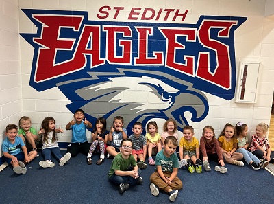 Several preschool children sitting in front of the St. Edith Eagles Logo